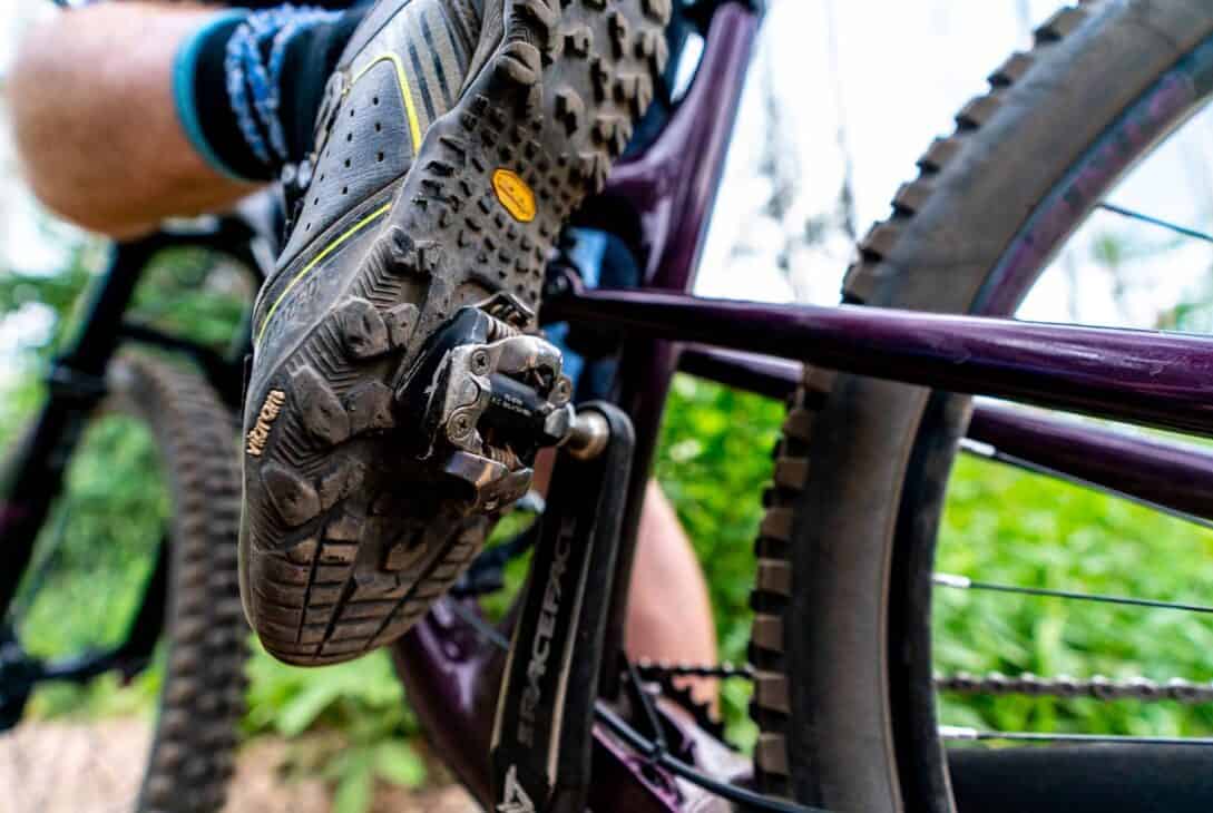 Sapato de ciclismo mountain bike com detalhe de pedal clip pedalando em trilha outdoor.