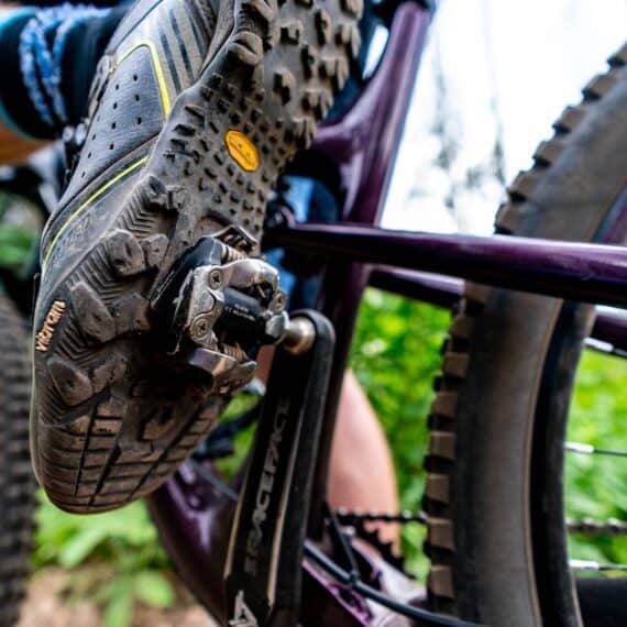 Sapato de ciclismo mountain bike com detalhe de pedal clip pedalando em trilha outdoor.