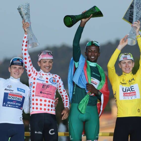 Primeiro lugar no Tour de France 2024 com ciclistas comemorando no pódio e troféus na mão.