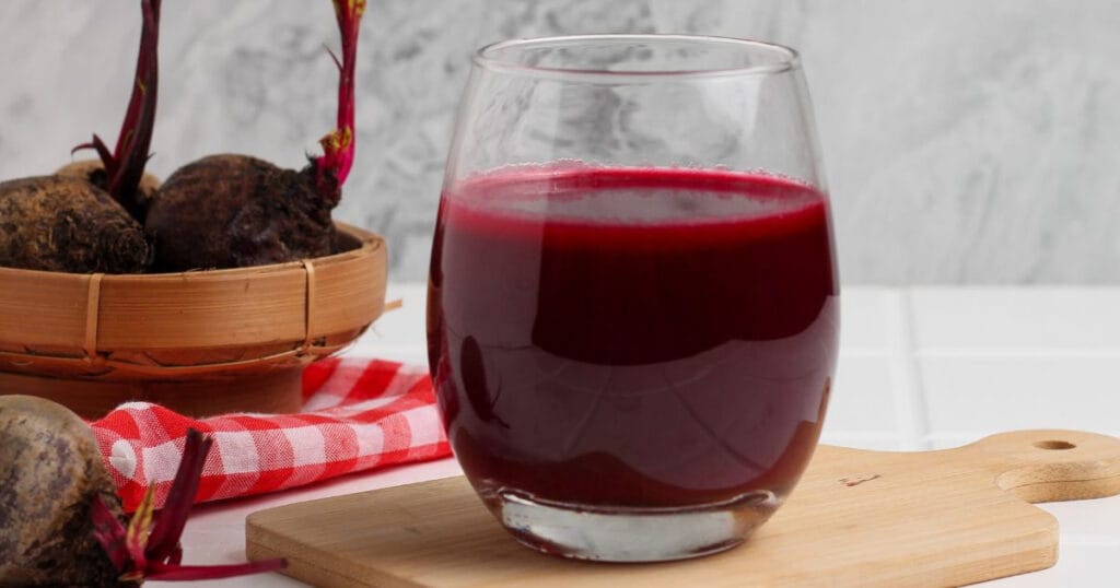 Um copo com suco de beterraba com algumas beterrabas ao fundo.