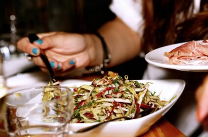 Uma mulher comendo um prato de saladas com um prato ao lado de presunto.