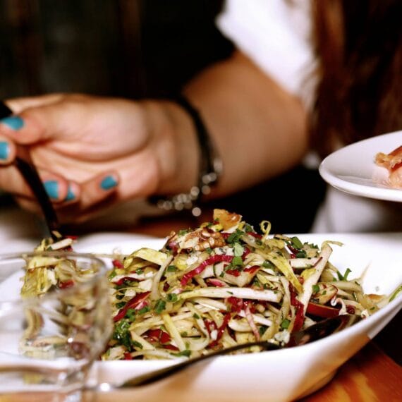 Uma mulher comendo um prato de saladas com um prato ao lado de presunto.