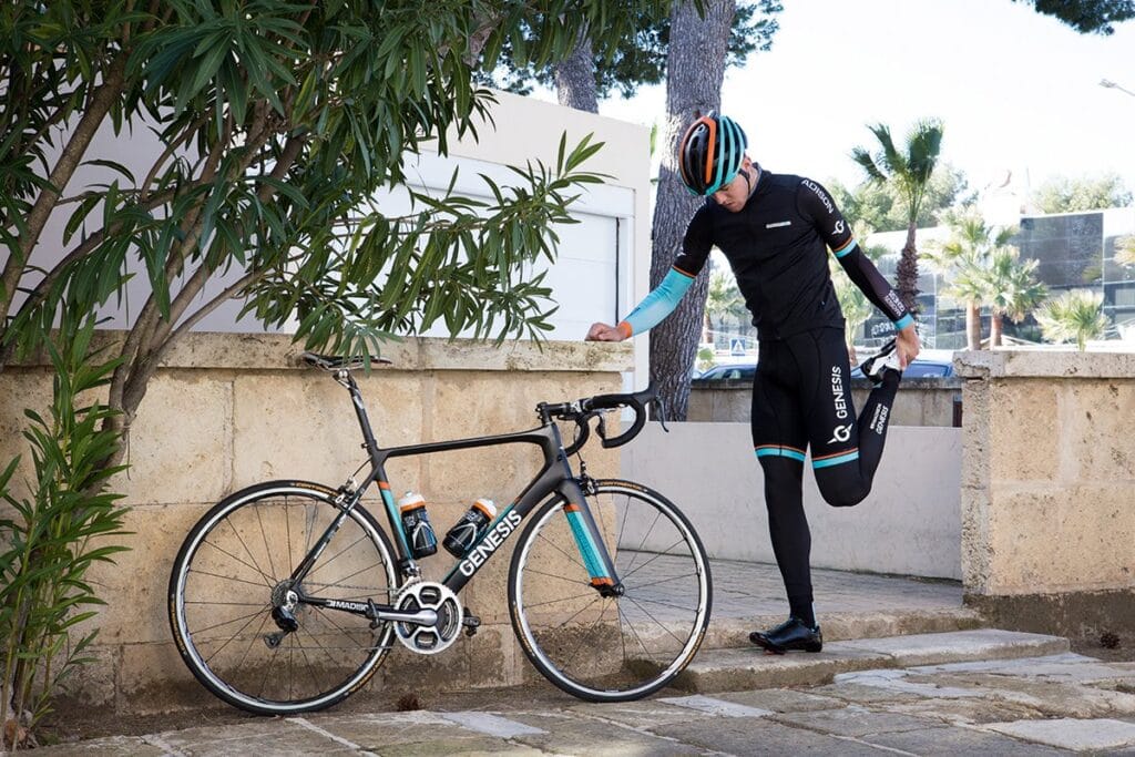 Ciclista se alongando apoiado em sua bike em uma avenida.
