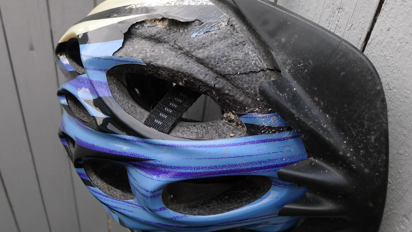Capacete de ciclismo azul e preto com a casca rachada e o isopor esmagado após uma queda