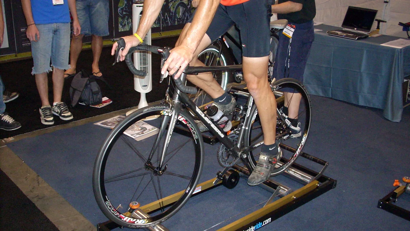 Ciclista equilibra a bicicleta sobre um rolo de rolos durante evento, com público ao fundo