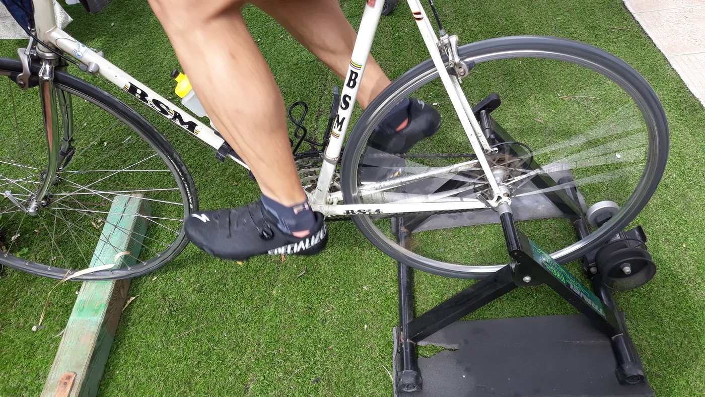 Ciclista pedala uma bicicleta de estrada encaixada num rolo de treino montado sobre a grama