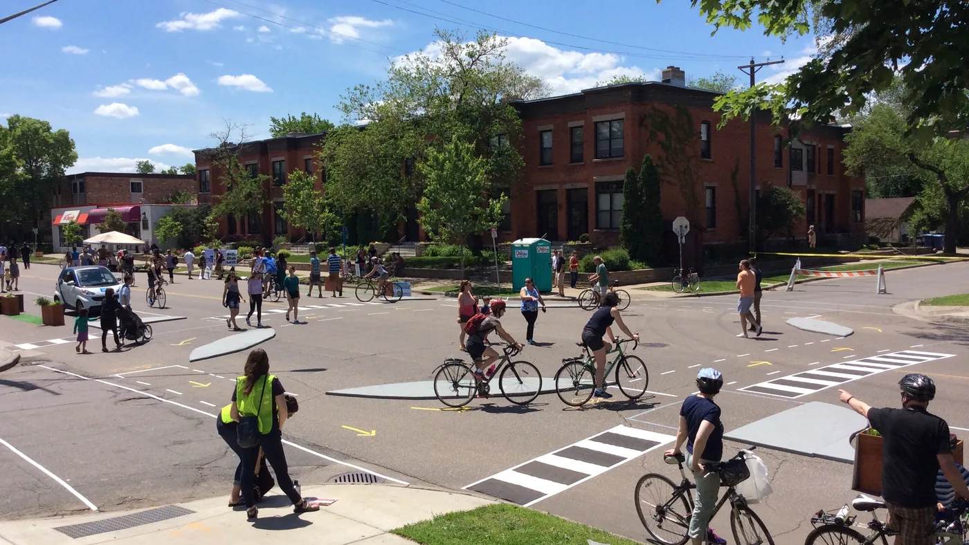 Ciclistas e pedestres circulam em cruzamento urbano com faixa exclusiva para bicicletas
