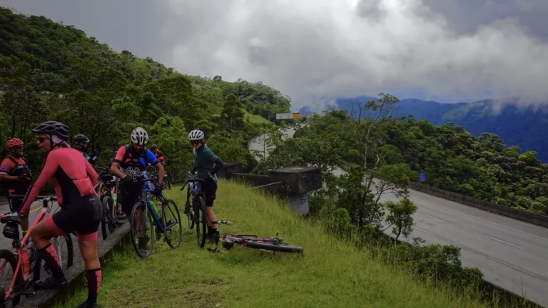 Grupo de ciclistas parado no alto da Rota Márcia Prado, na Serra do Mar, com a Rodovia dos Imigrantes visível no vale abaixo