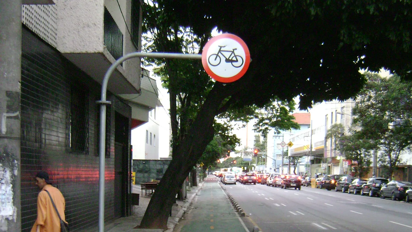 Ciclovia segregada construída ao lado da calçada em Belo Horizonte, com placa de regulamentação de circulação exclusiva de bicicletas e um pedestre caminhando no passeio