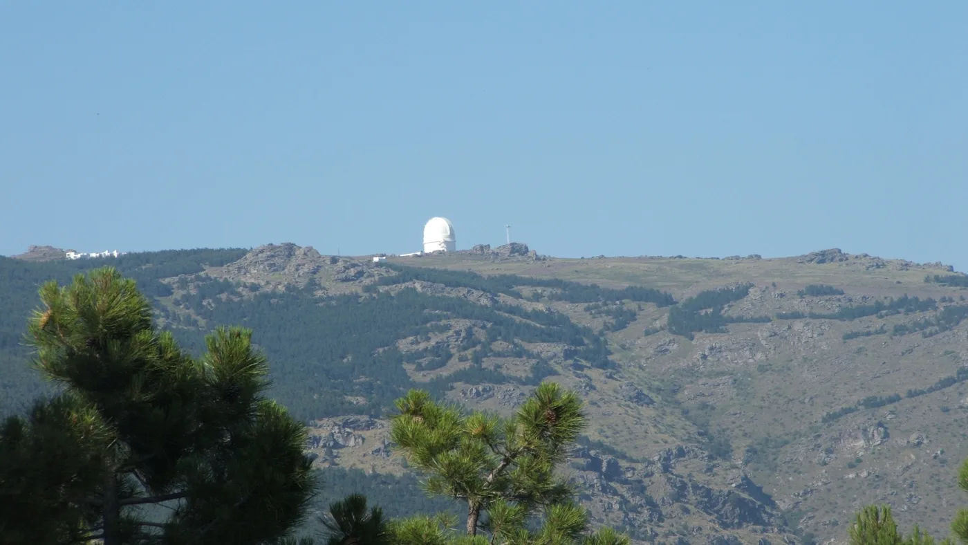 Cúpula branca do observatório de Calar Alto no alto da serra, vista de longe entre pinheiros, em Almería