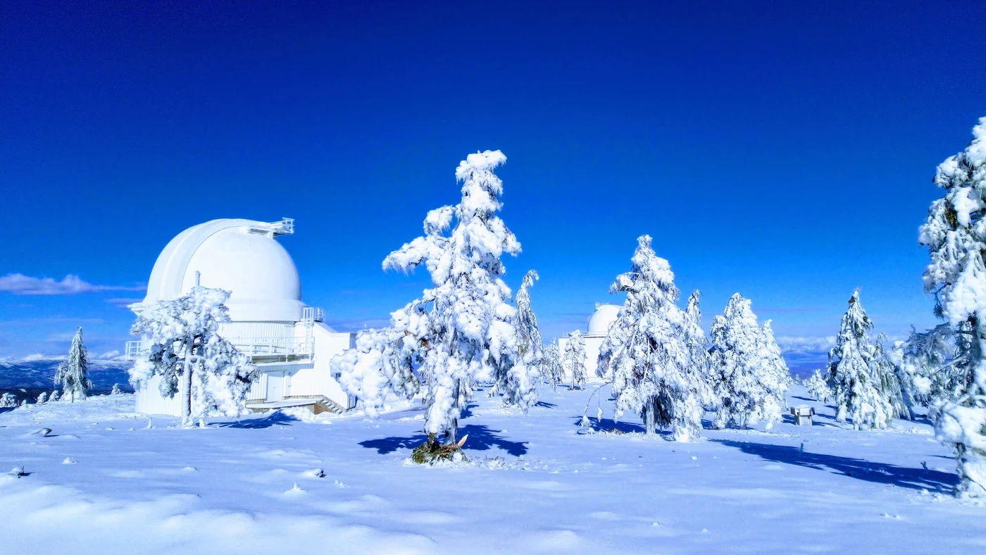 Cúpulas brancas do observatório astronômico do Calar Alto cobertas de neve a 2.168 m de altitude, com pinheiros congelados e céu azul intenso ao redor
