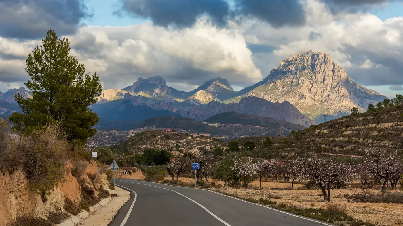 Estrada CV-775 serpenteia entre amendoeiras com a Serra de Aitana ao fundo, em Relleu, Alicante