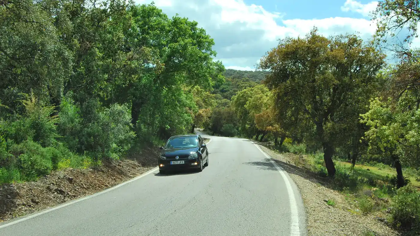 Estrada estreita entre azinheiras, com um carro na pista, perto de Grazalema, no trecho andaluz onde a Volta a Espanha 2026 corre 10 das 21 etapas