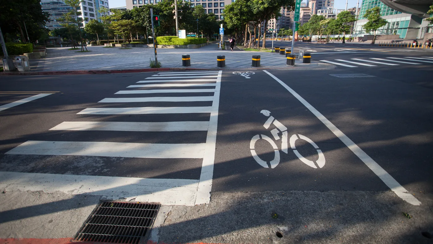 Faixa de pedestres zebrada com uma travessia exclusiva para bicicletas pintada ao lado, marcada com o símbolo de uma bicicleta, em cruzamento urbano