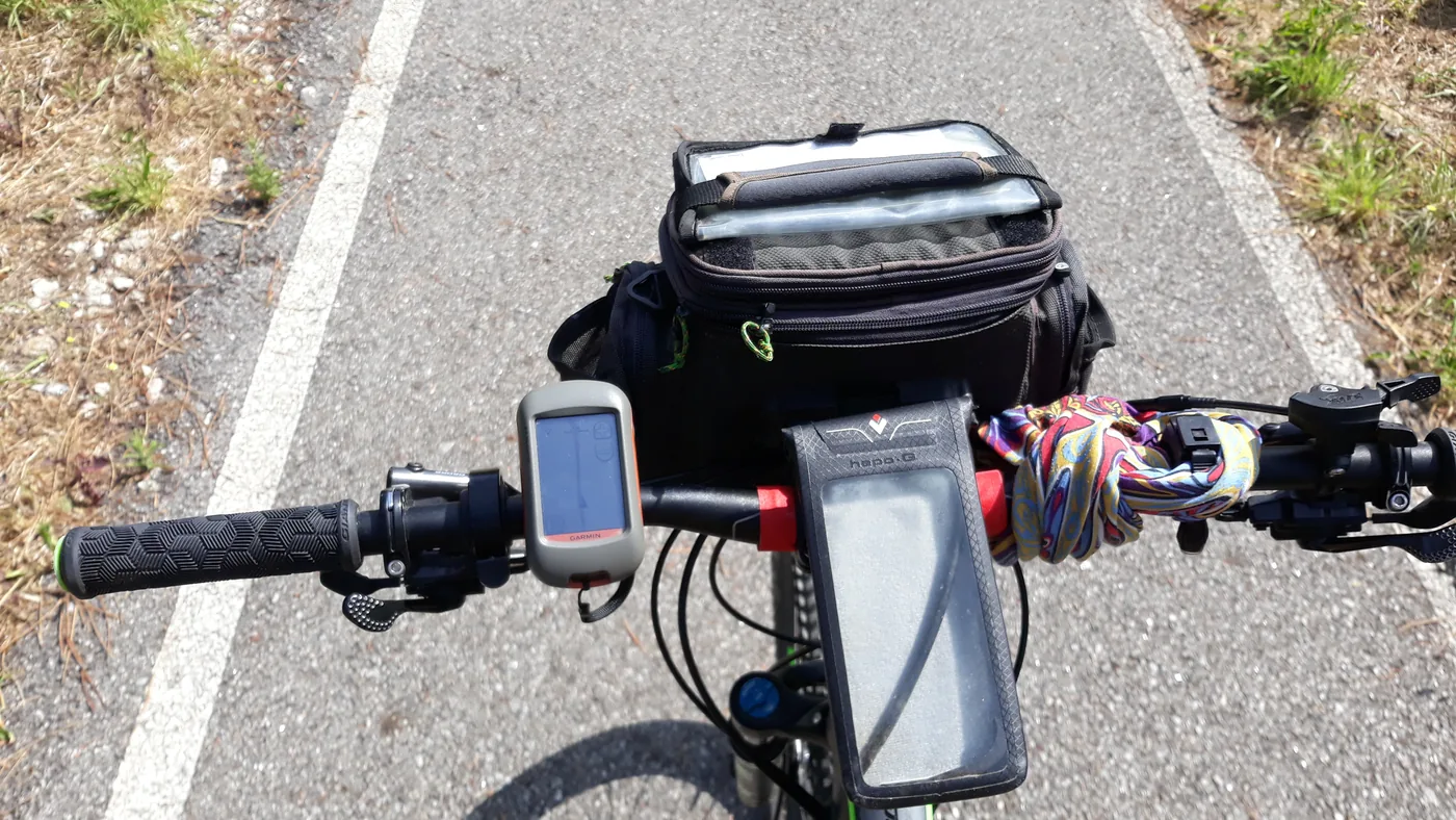 Guidão com aparelho de GPS, suporte de celular e bolsa de guidão, numa ciclovia