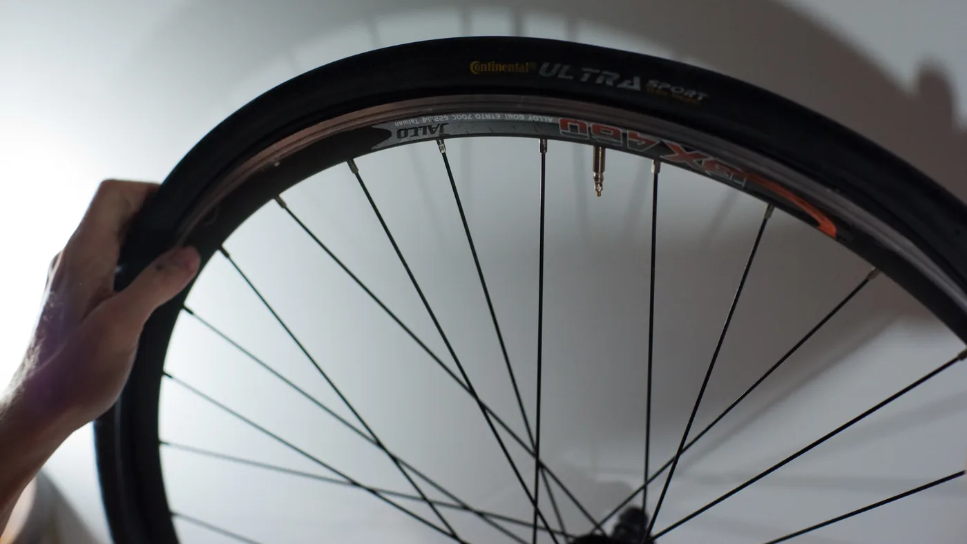 Mãos seguram uma roda de bicicleta com o pneu montado, vista de perto contra fundo claro