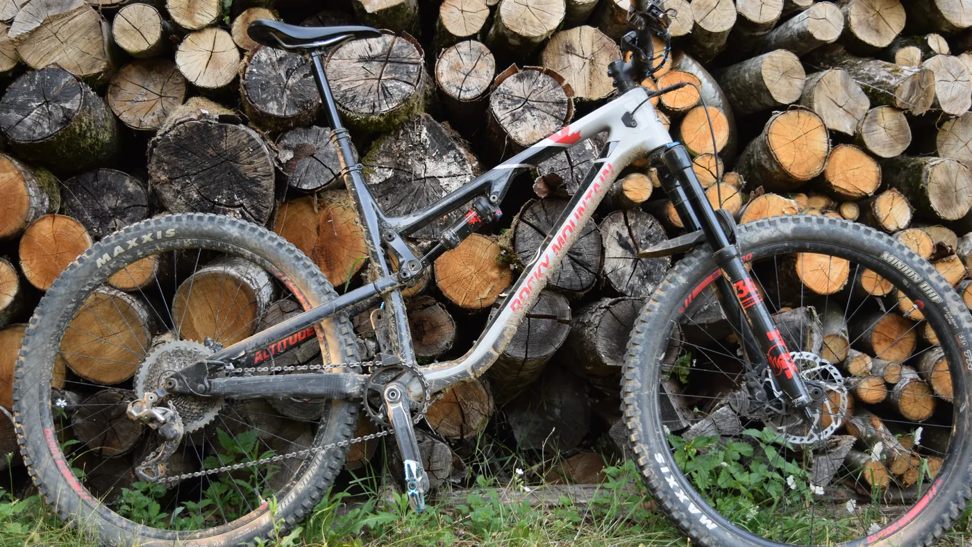 Mountain bike de suspensão dupla apoiada numa pilha de lenha, com pneus largos e freio a disco