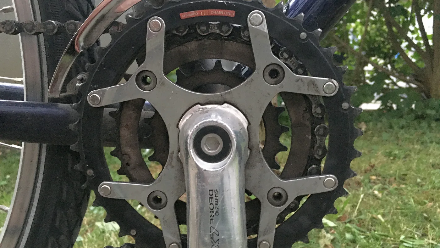 Pedivela com duas coroas visto de perto, com o pedal e o quadro ao fundo