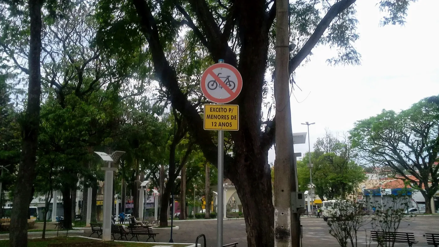 Placa de regulamentação R-12, círculo vermelho com bicicleta cortada, indicando proibição de trânsito de bicicletas, com placa complementar "exceto para menores de 12 anos"