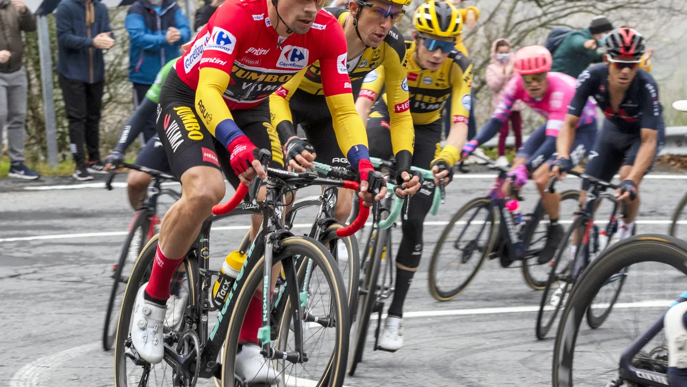 Primož Roglič de camisa vermelha pedala à frente do pelotão numa subida com torcida na beira da estrada, na Vuelta 2020