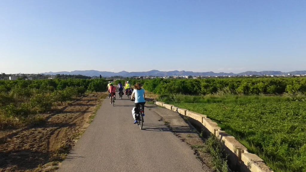 Ciclistas pedalam por estrada rural com montanhas ao fundo