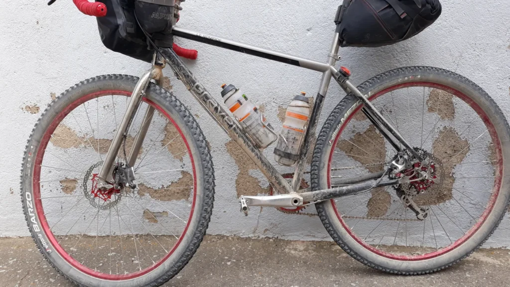 Bicicleta gravel com bolsas de bikepacking enlameada, apoiada após pedal em estrada de terra