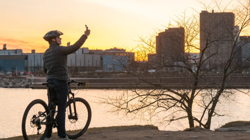 Ciclista com sua bike tirando uma foto no por do sol de uma grande cidade.