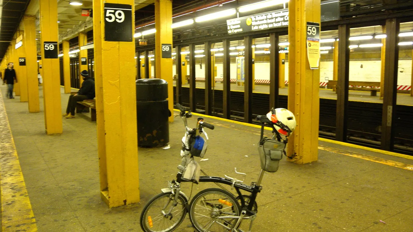 Bicicleta dobrável semidobrada em plataforma de metrô, com capacete e alforje pendurados no selim