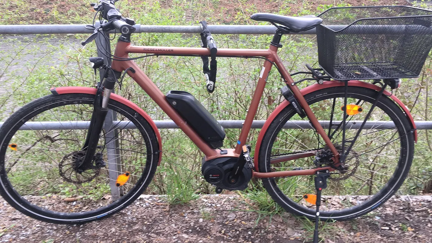 Bicicleta elétrica de pedal assistido com motor central, bateria no quadro, farol dianteiro e refletores nas rodas e pedais