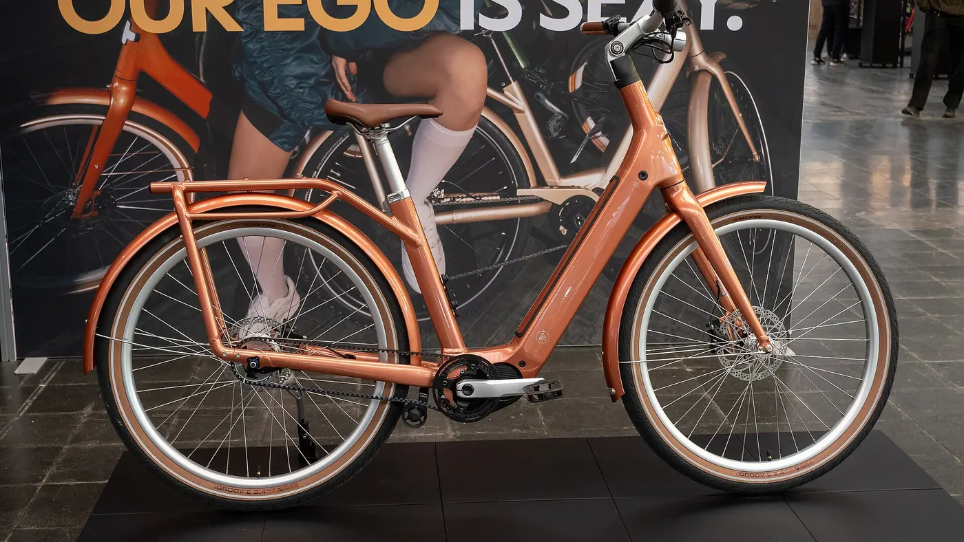 Bicicleta elétrica urbana de pedal assistido exposta sobre um pedestal, com bateria integrada ao quadro