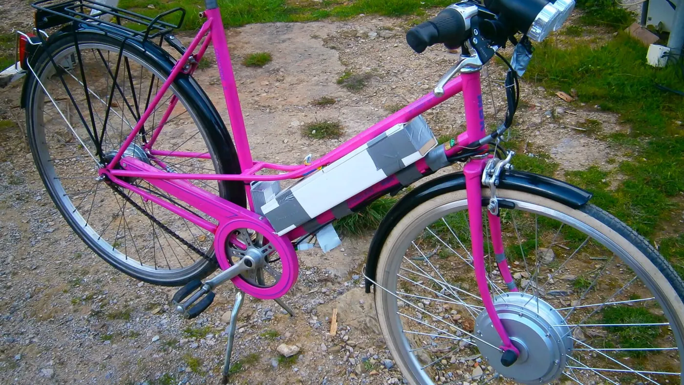 Bicicleta urbana antiga convertida com kit elétrico: motor de cubo dianteiro e bateria improvisada presa ao quadro com fita