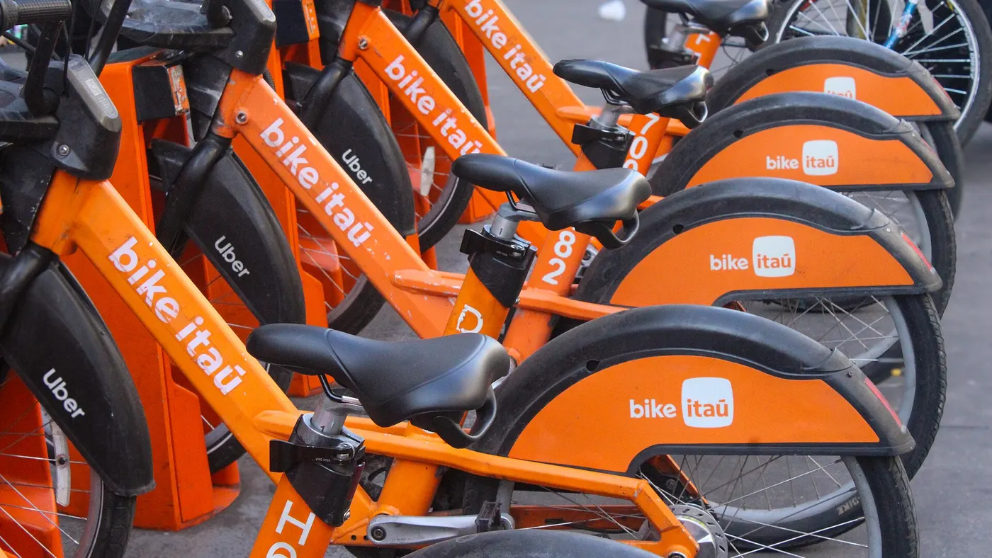 Fileira de bicicletas mecânicas laranja do Bike Itaú em estação na Avenida Paulista, sistema operado pela Tembici