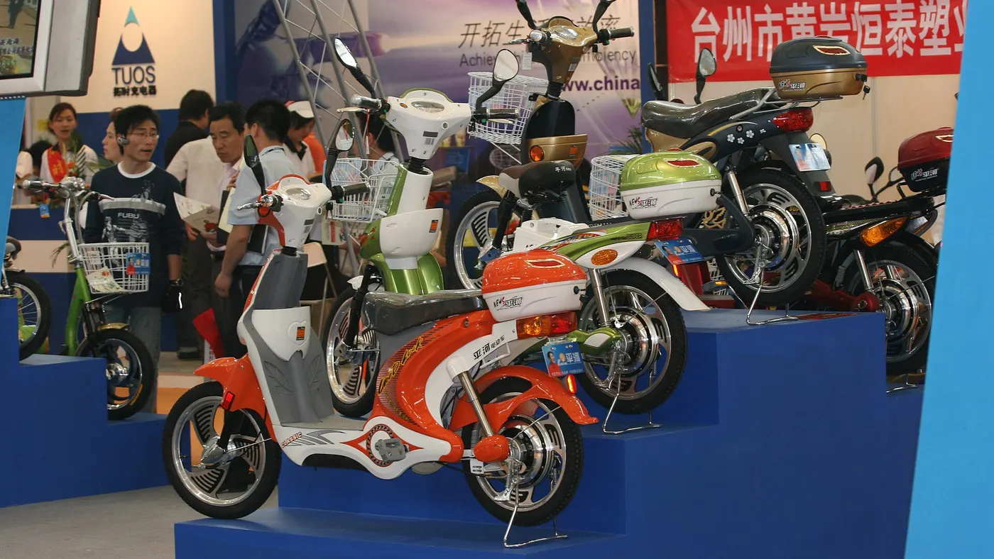 Modelos estilo scooter com retrovisores e baú expostos numa feira de veículos elétricos na China, do tipo vendido como bicicleta elétrica