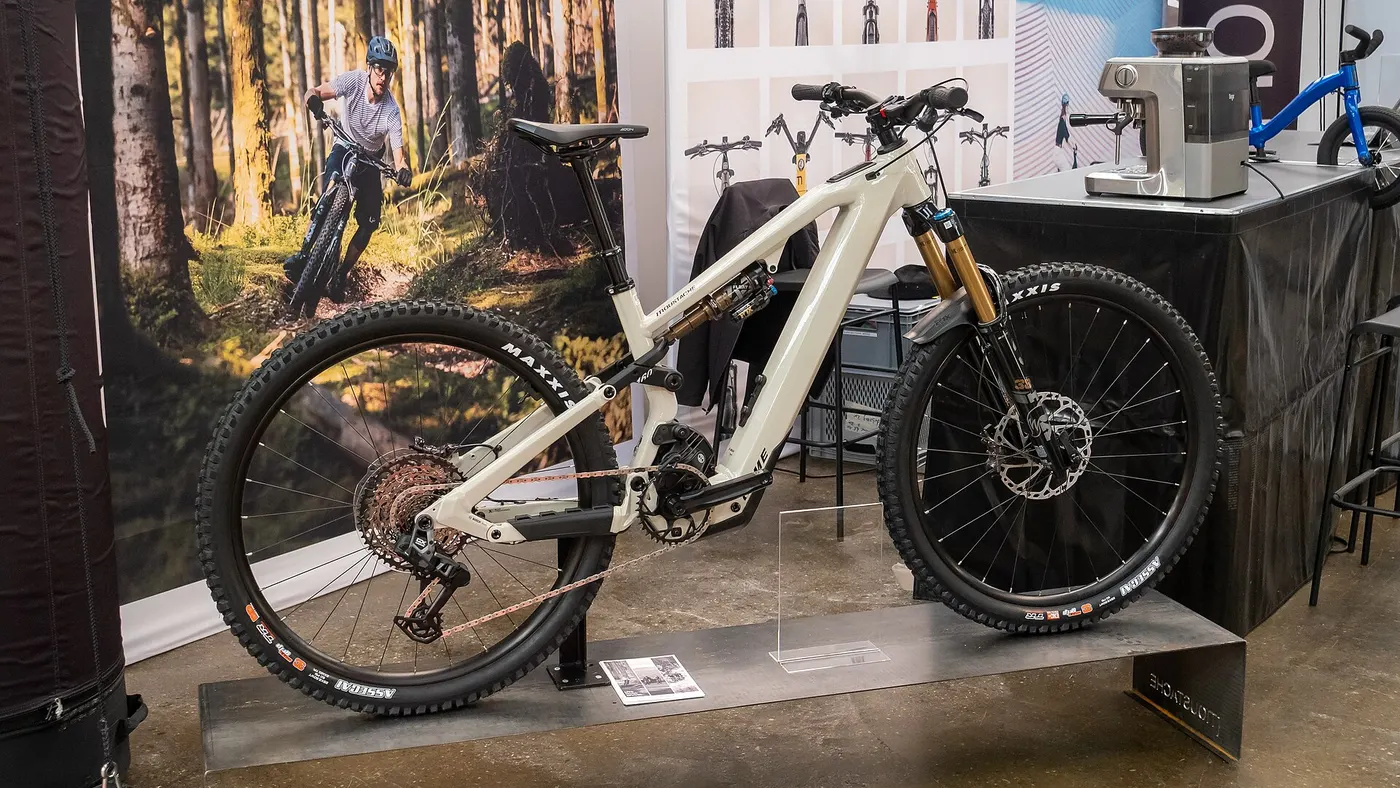 Mountain bike elétrica de suspensão total exposta em estande de feira, com motor central e bateria integrada ao quadro